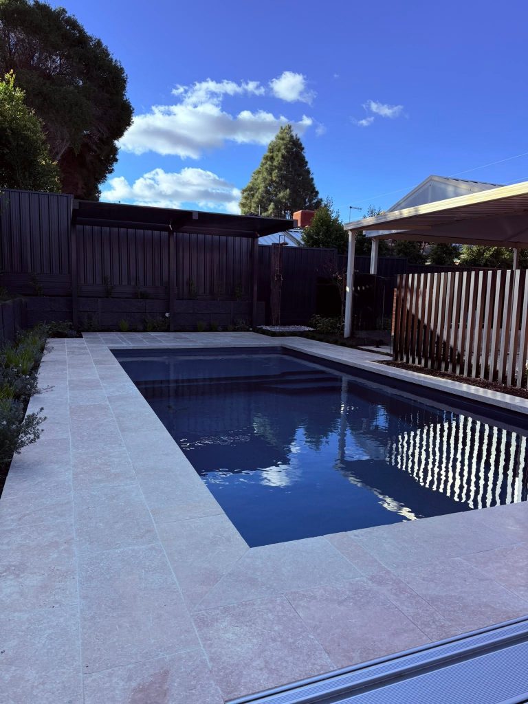 Finished swimming pool installation in Dubai with dark tile finish, wide travertine deck and a shaded pergola seating area